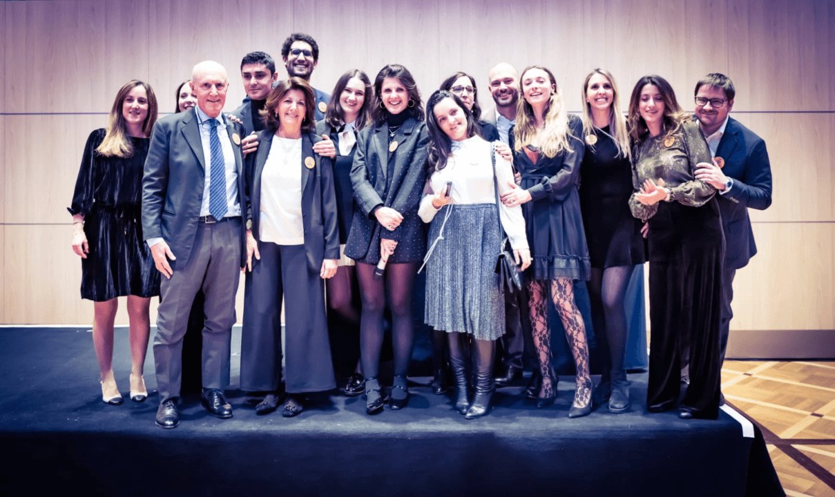 Un gruppo di una ventina di persone in posa sul palco, davanti a una parete di legno chiaro.