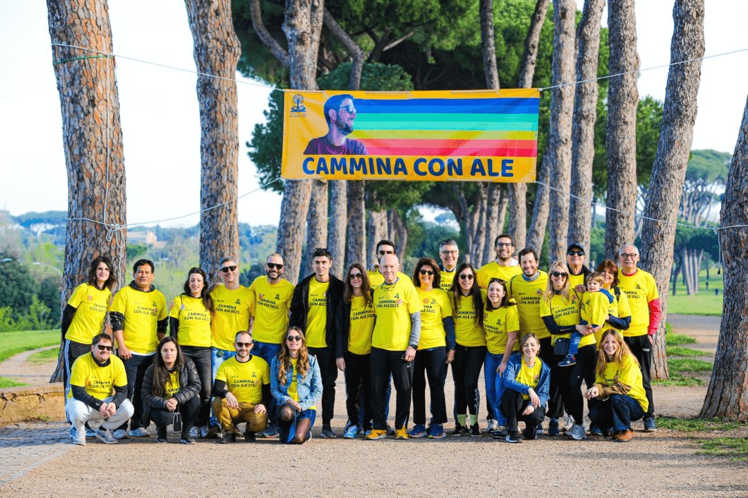 Una trentina di volontari con la maglietta gialla in posa sotto lo striscione della Cammina con Ale, tra i pini.