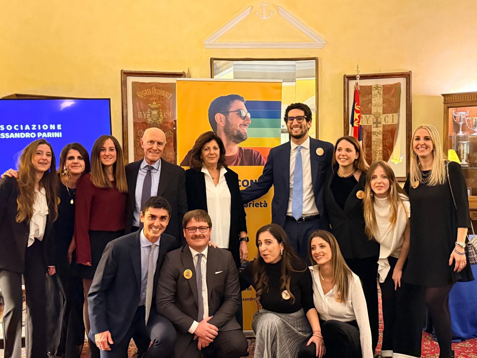 Una ventina di persone in abito elegante in posa davanti a uno schermo con il logo dell'associazione, in un salone del Circolo Tevere Remo.